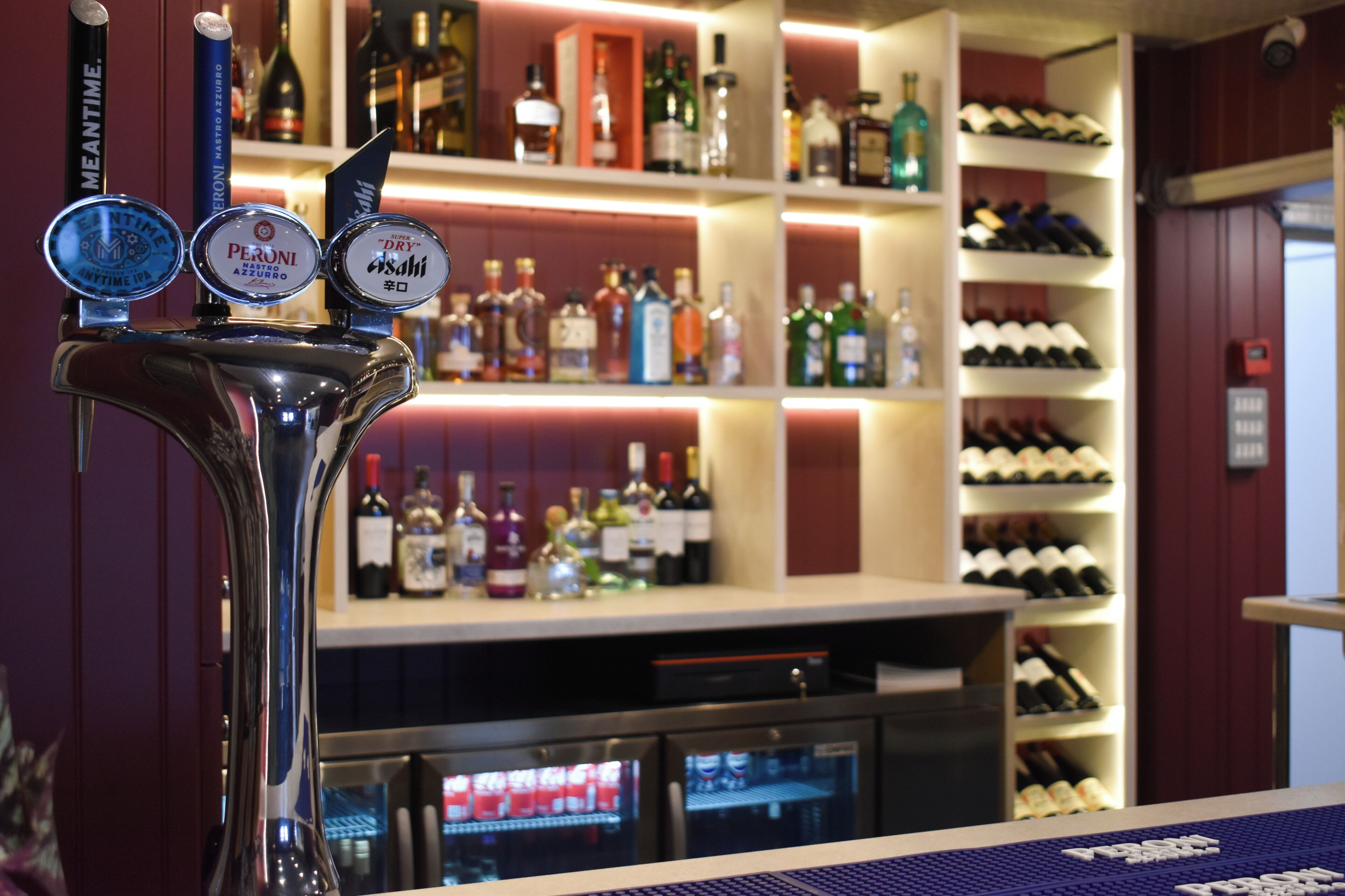 Un espace bar avec un robinet, des étagères remplies de bouteilles d’alcool et un présentoir réfrigéré.