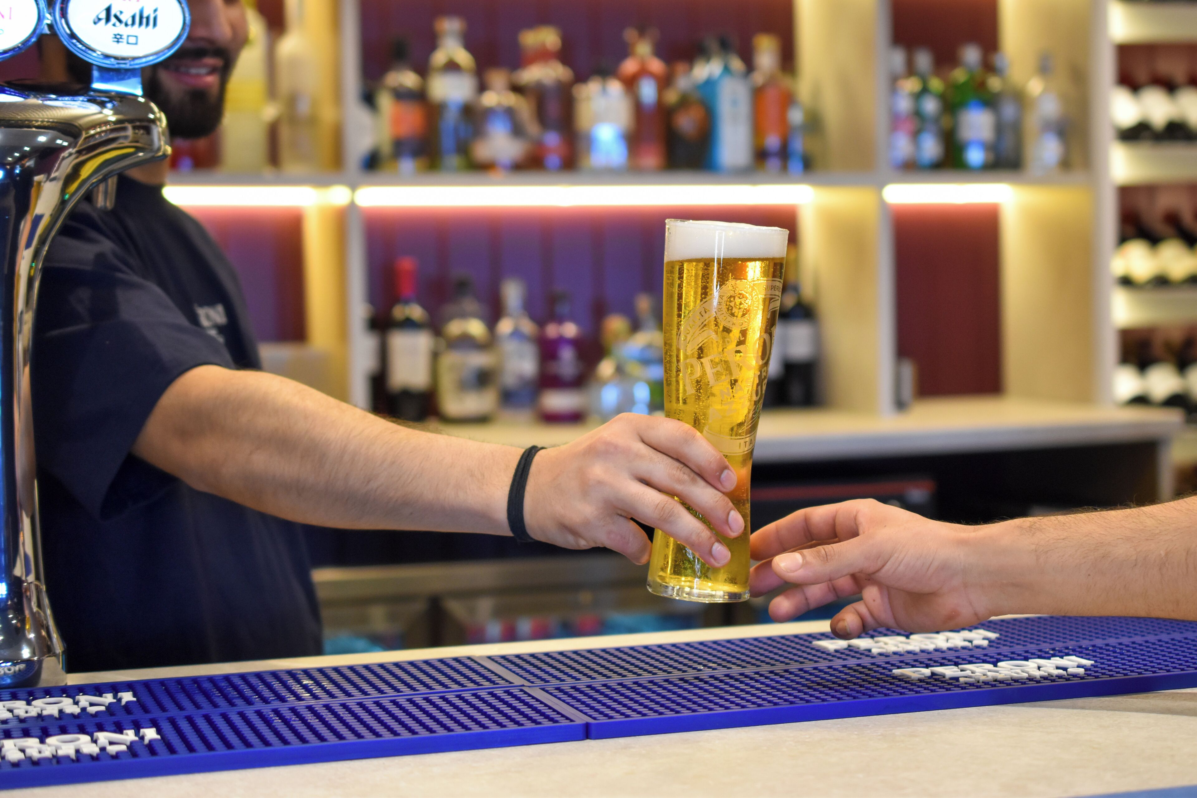 A bar with a tap labeled 'Asahi' and a bartender serving a beer.