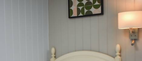 A neatly made bed with white bedding, a headboard, and a wall-mounted lamp.