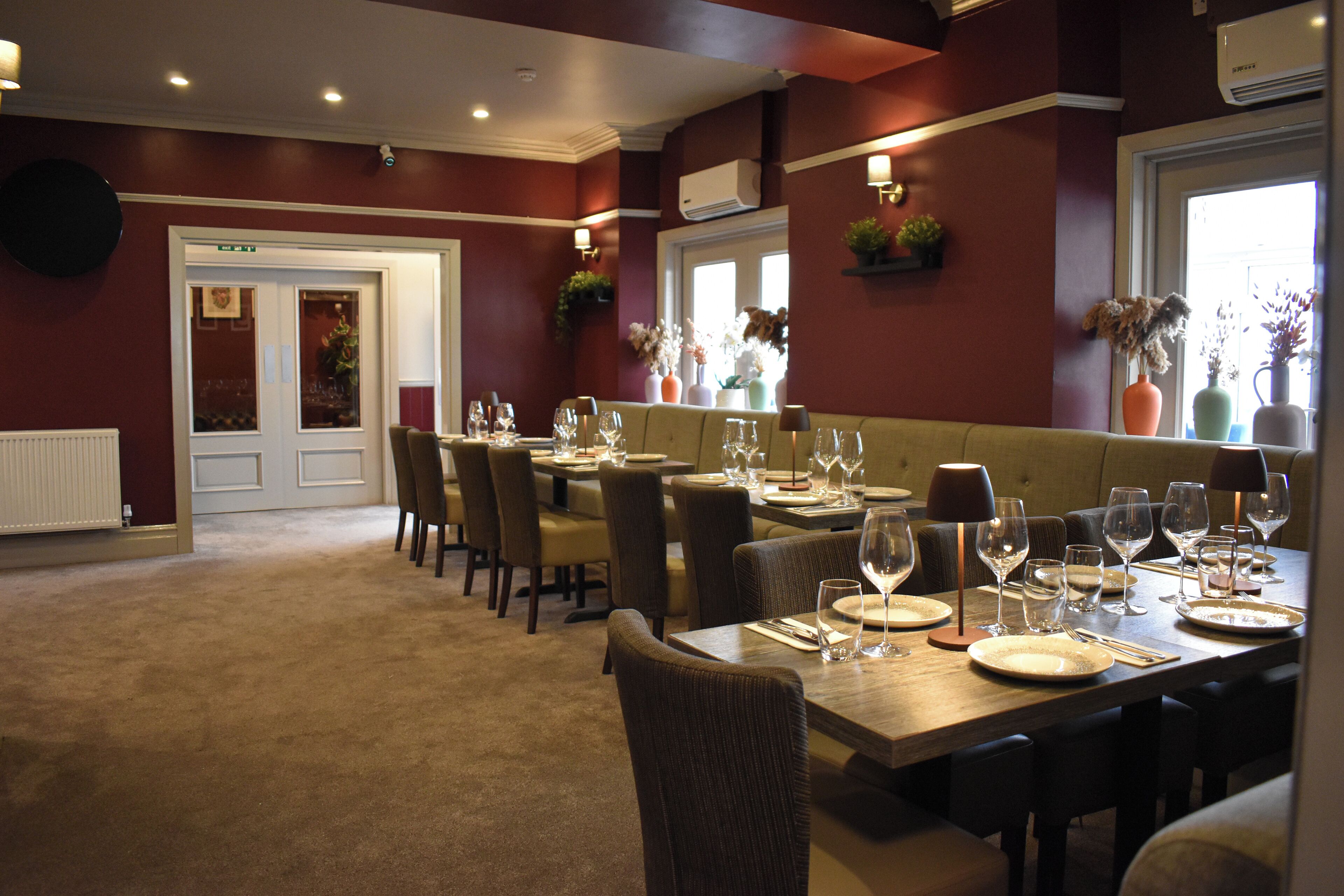A dining area with tables set for a meal, chairs, and decorative plants.