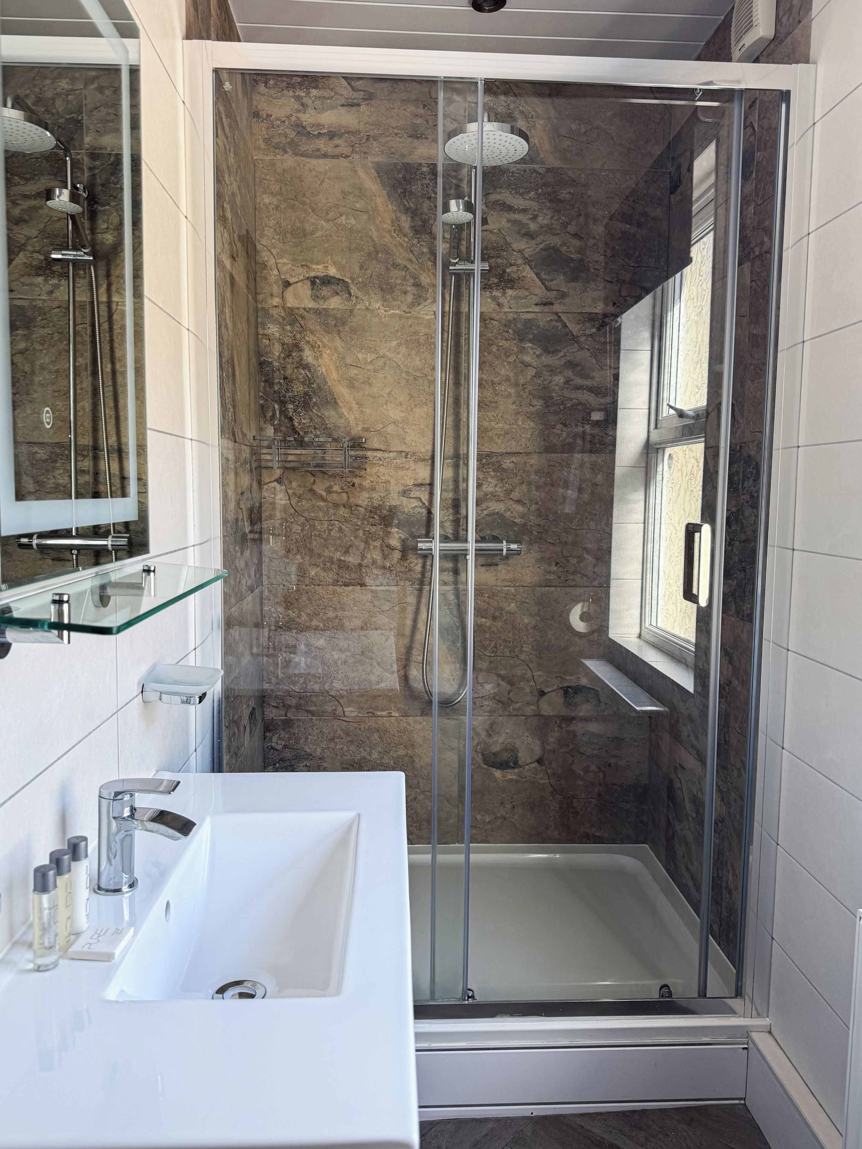 A modern bathroom with a glass-enclosed shower, a white sink, and a mirror.