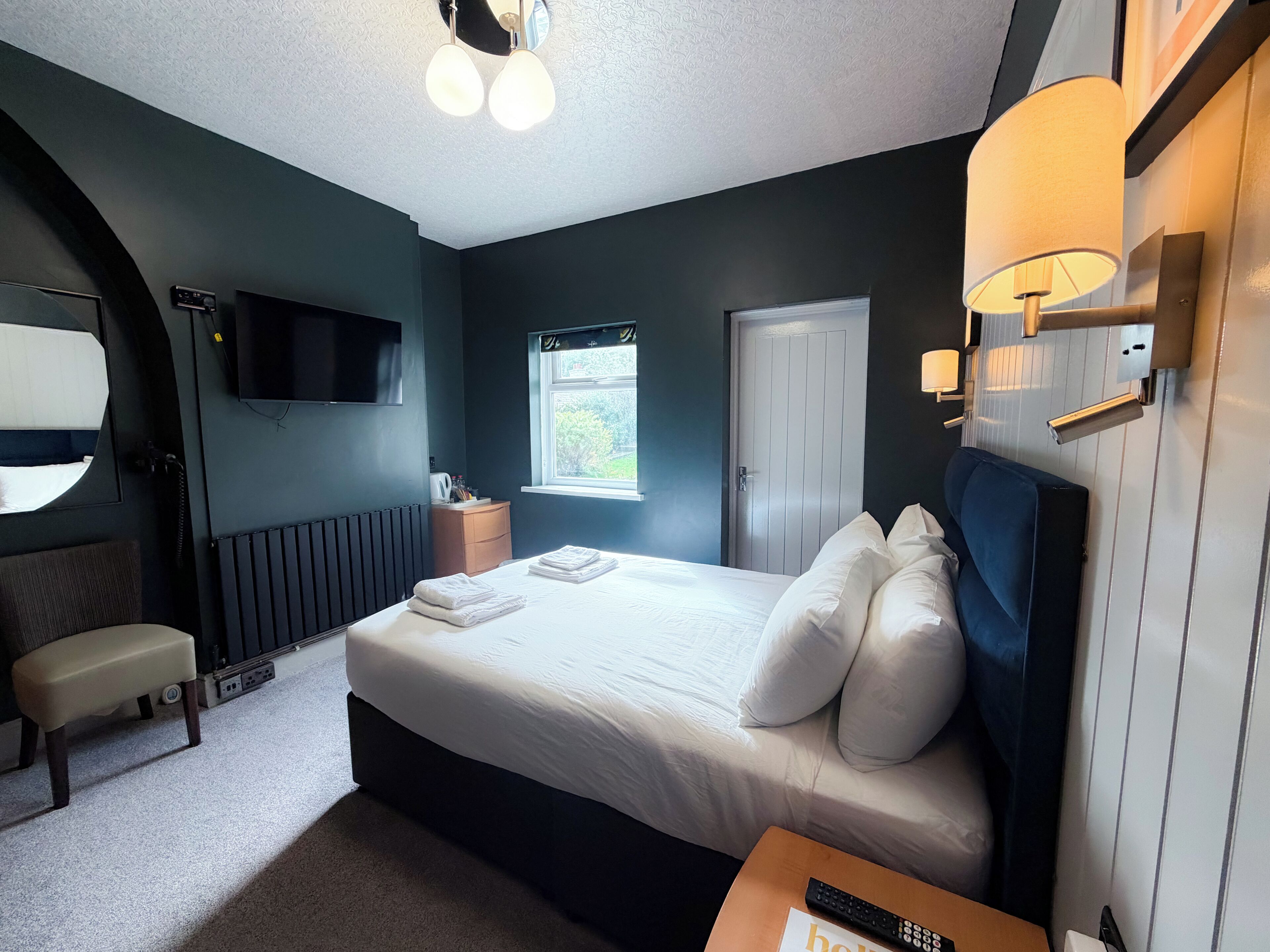 A hotel room with a bed, bedside table, lamp, and a TV mounted on the wall.
