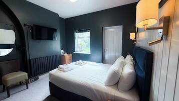 A hotel room with a bed, bedside table, lamp, and a TV mounted on the wall.