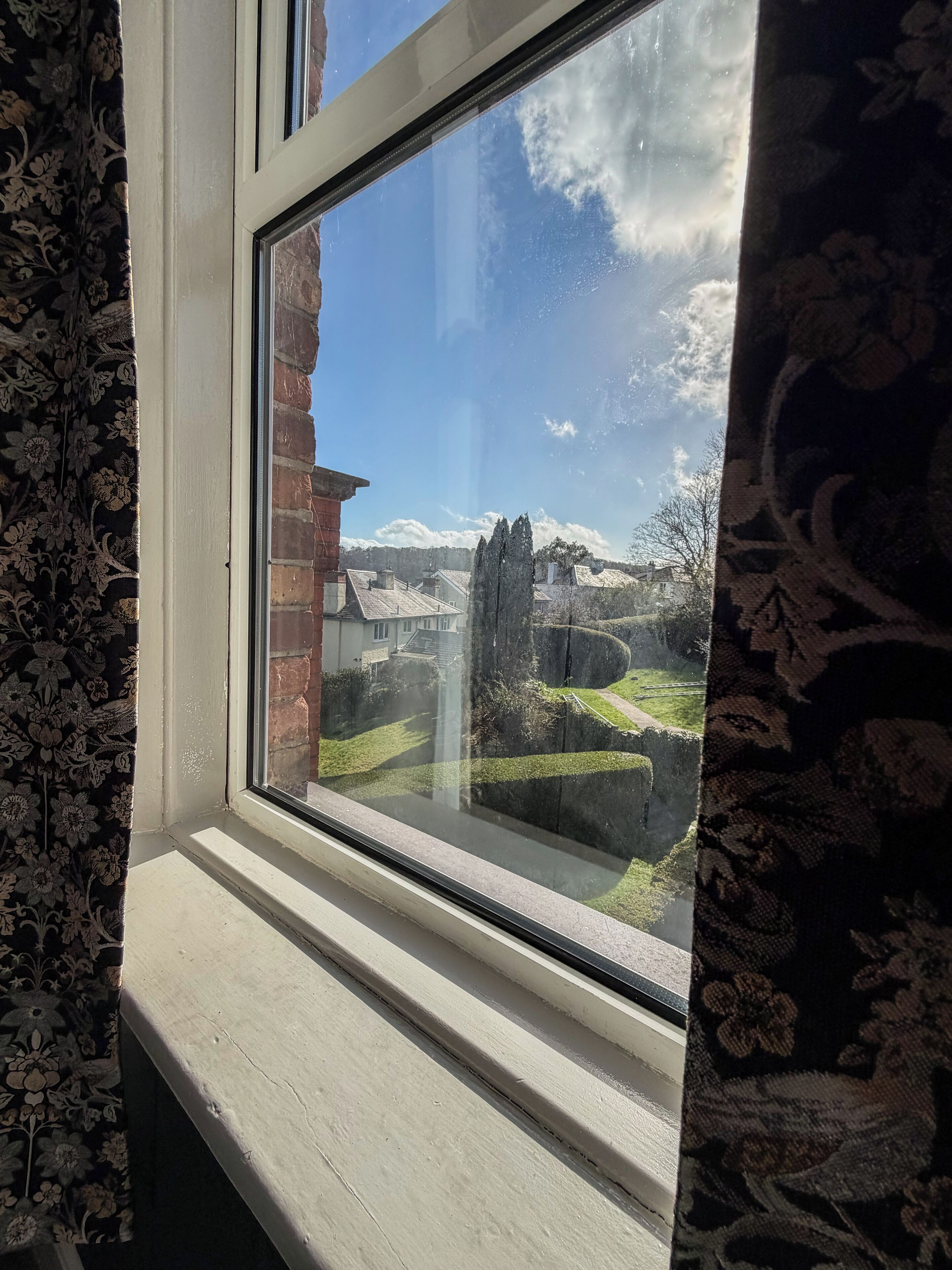 A window with a view of a brick building, a grassy area, and a clear sky.