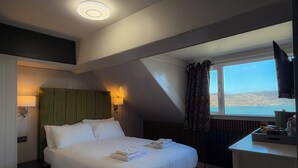 Habitación de hotel con cama, escritorio, televisor, ventana con vistas y una lámpara en el techo.