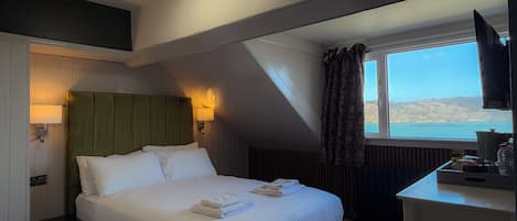 A hotel room with a bed, a desk, a television, a window with a view, and a ceiling light.