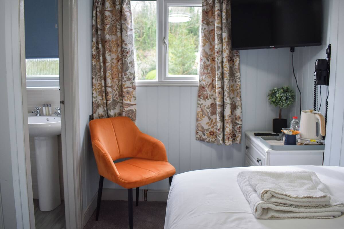 Habitación de hotel con cama, una silla, lavamanos, televisor y ventana con cortinas.
