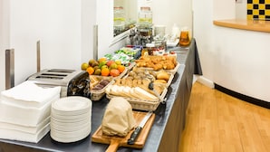 Un buffet proposant une variété de plats, notamment des fruits, des pâtisseries et du pain, disposés sur une table avec des assiettes et des couverts.