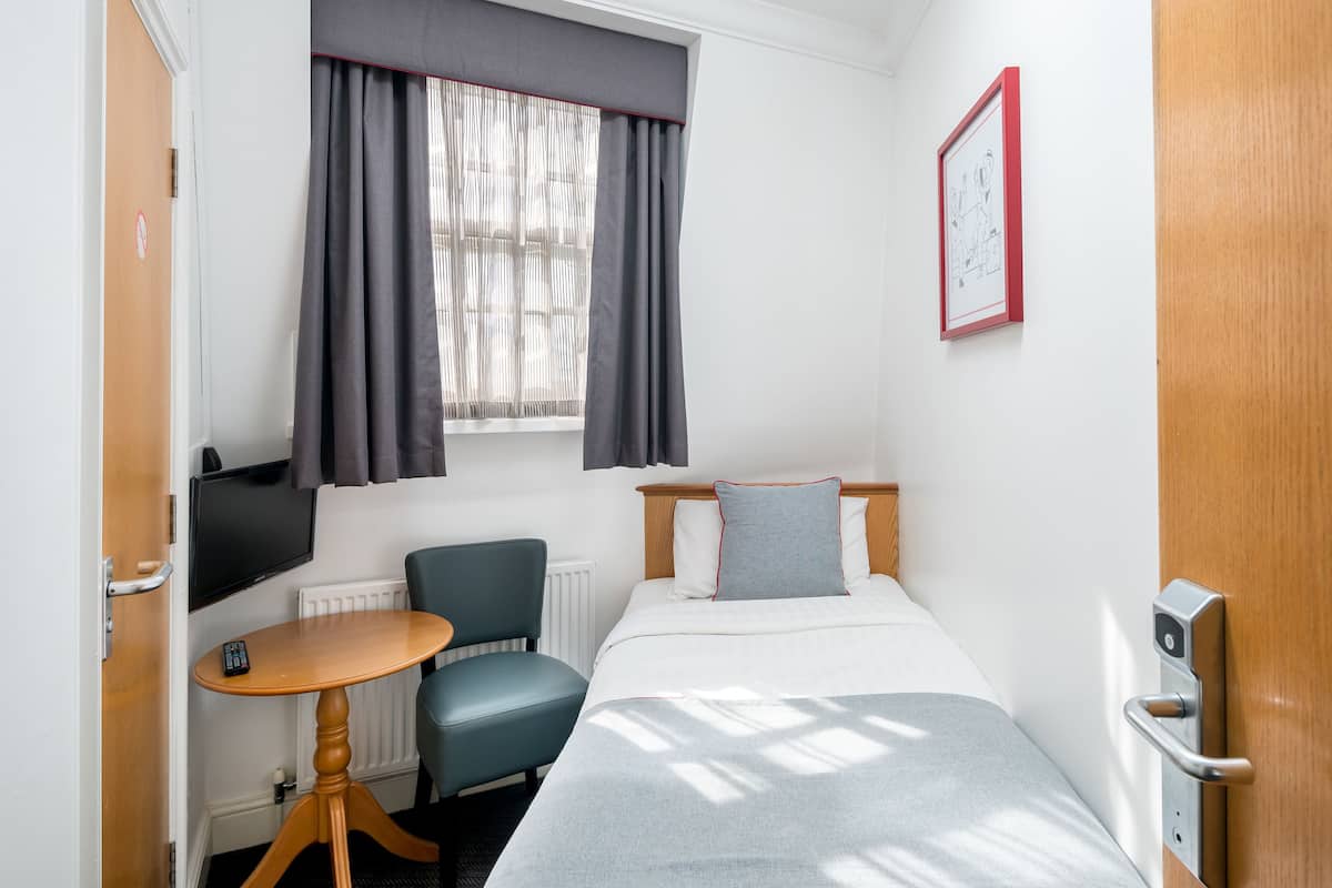Una habitación de hotel con cama, escritorio, silla, ventana con cortinas, radiador, televisor y puerta.