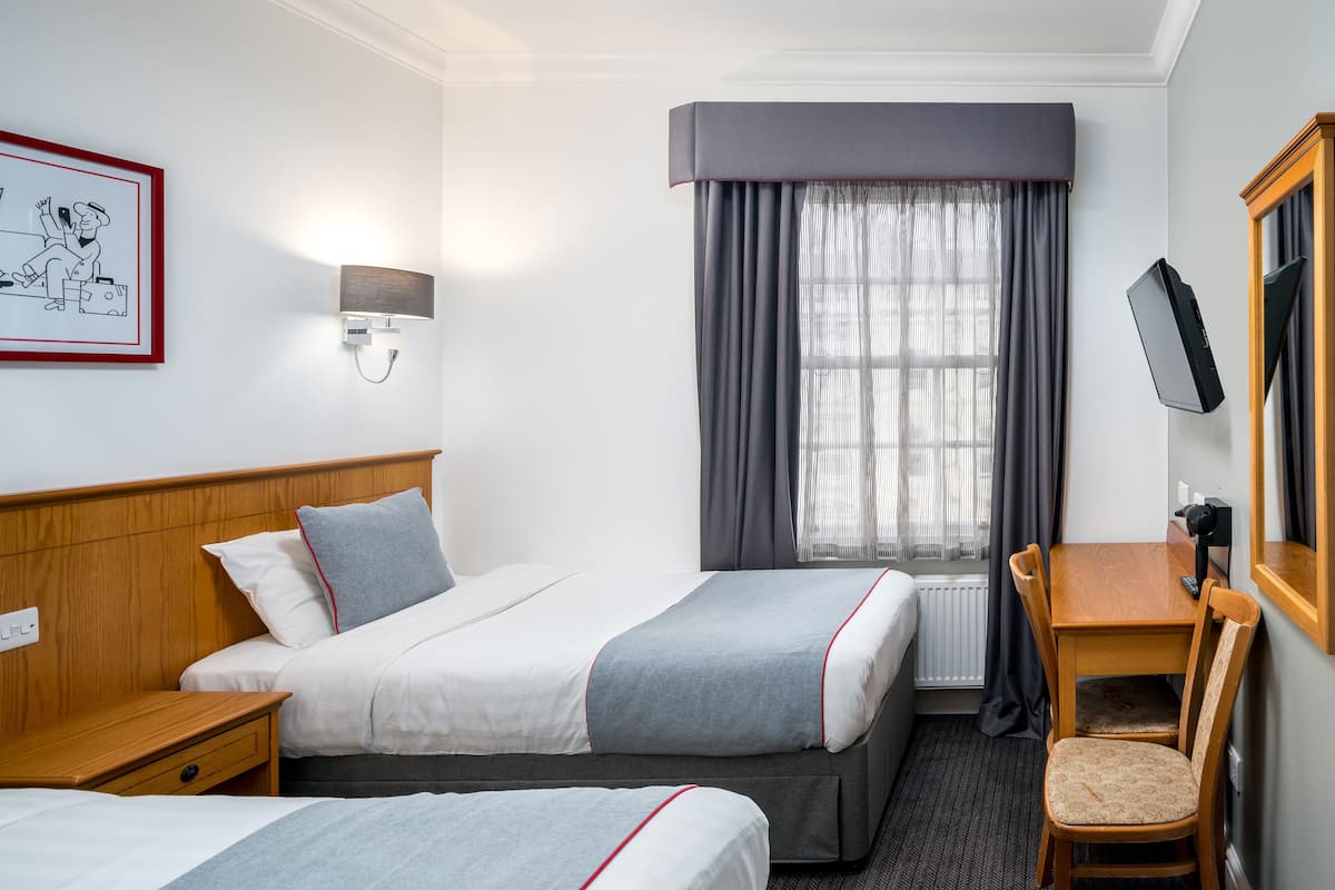 Habitación de hotel con dos camas, un escritorio, una silla, un televisor y una ventana con cortinas.
