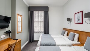 Une chambre d’hôtel avec deux lits, un bureau, une chaise, une télévision et une fenêtre avec des rideaux.