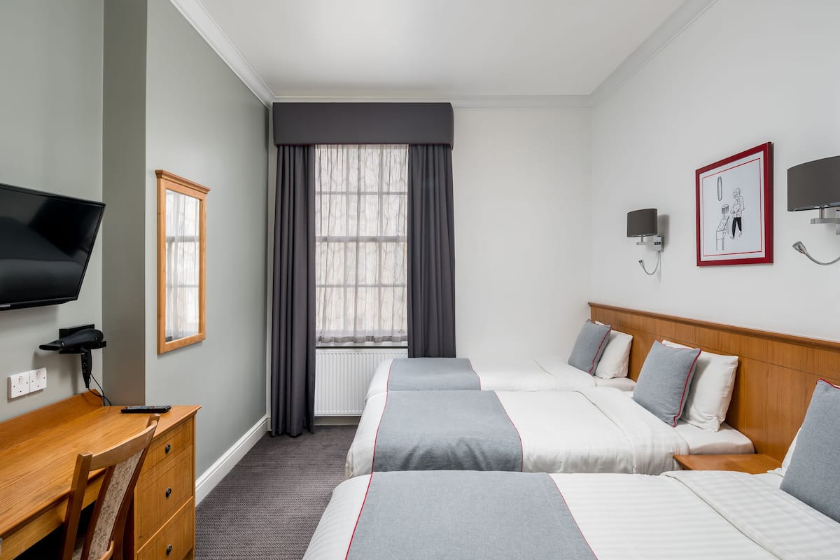 Una habitación de hotel con dos camas, un escritorio, una silla, un televisor y una ventana con cortinas.