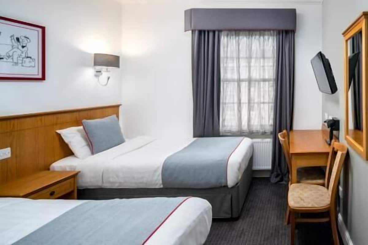 Habitación de hotel con dos camas, un escritorio, una silla, un televisor y una ventana con cortinas.