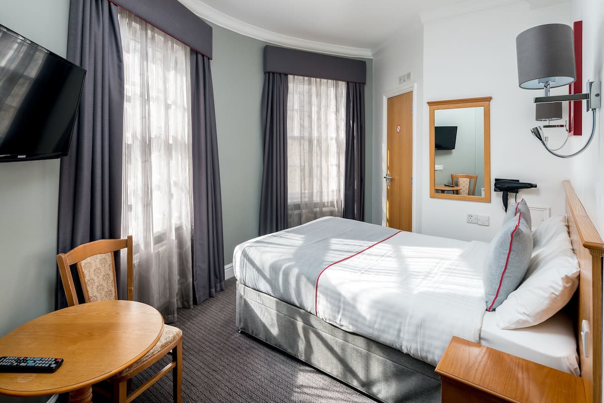 Una habitación de hotel con una cama, televisión, escritorio y una silla.