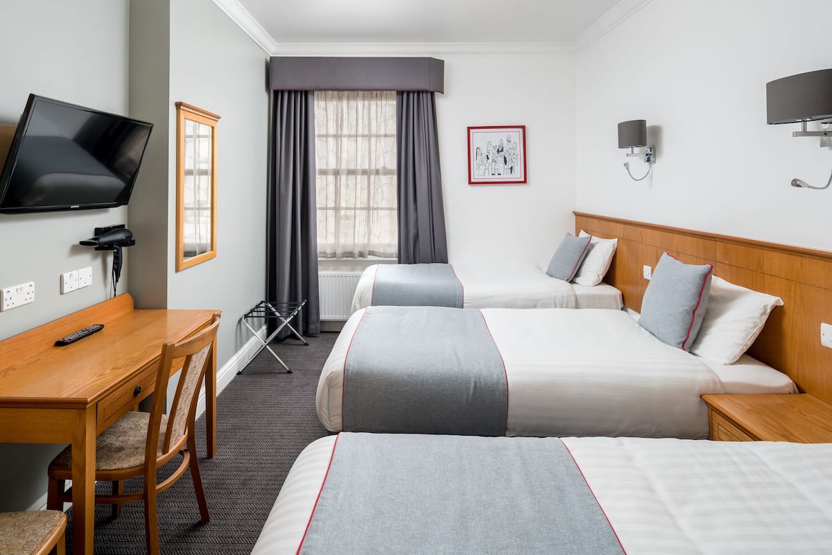 Habitación de hotel con dos camas, un escritorio, un televisor y una ventana con cortinas.