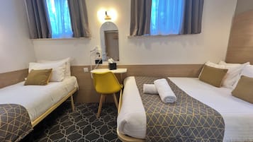 A hotel room with two single beds, a desk with a chair, a mirror, and a window with curtains.