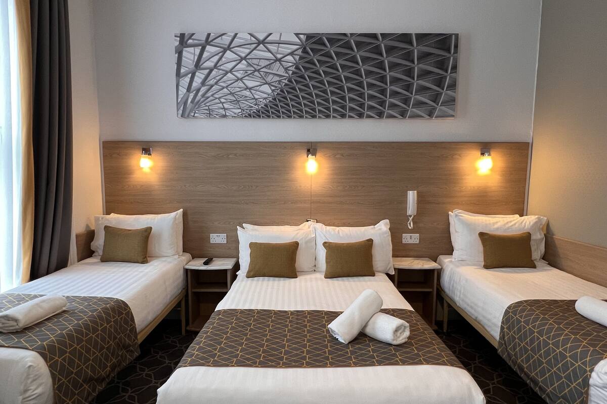 Ein Hotelzimmer mit drei Einzelbetten, einem großen Bett und einem modernen, abstrakten Kunstwerk über dem Kopfteil.