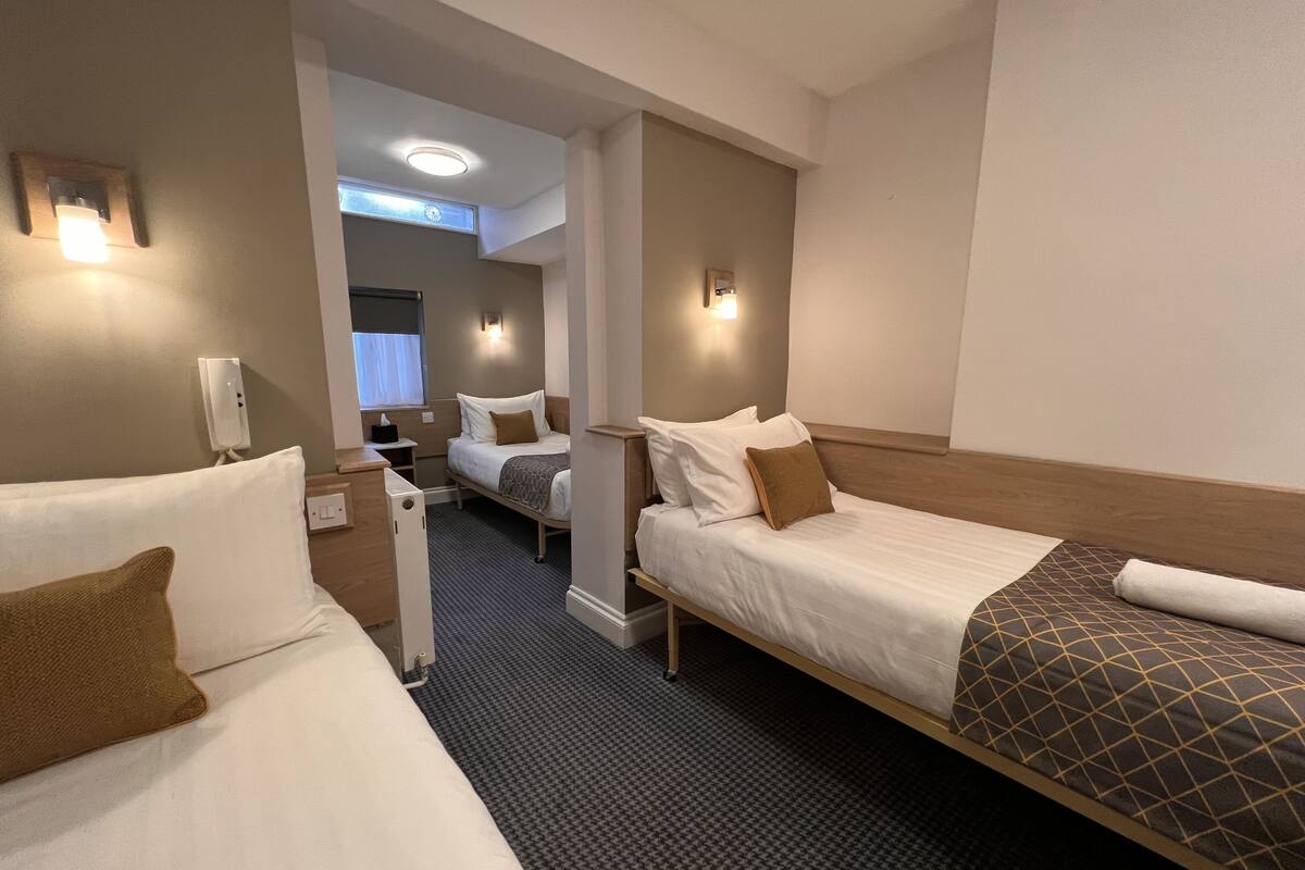 Ein Hotelzimmer mit zwei Betten, einem kleinen Schreibtisch, einem Telefon und einem Fenster mit Vorhängen.