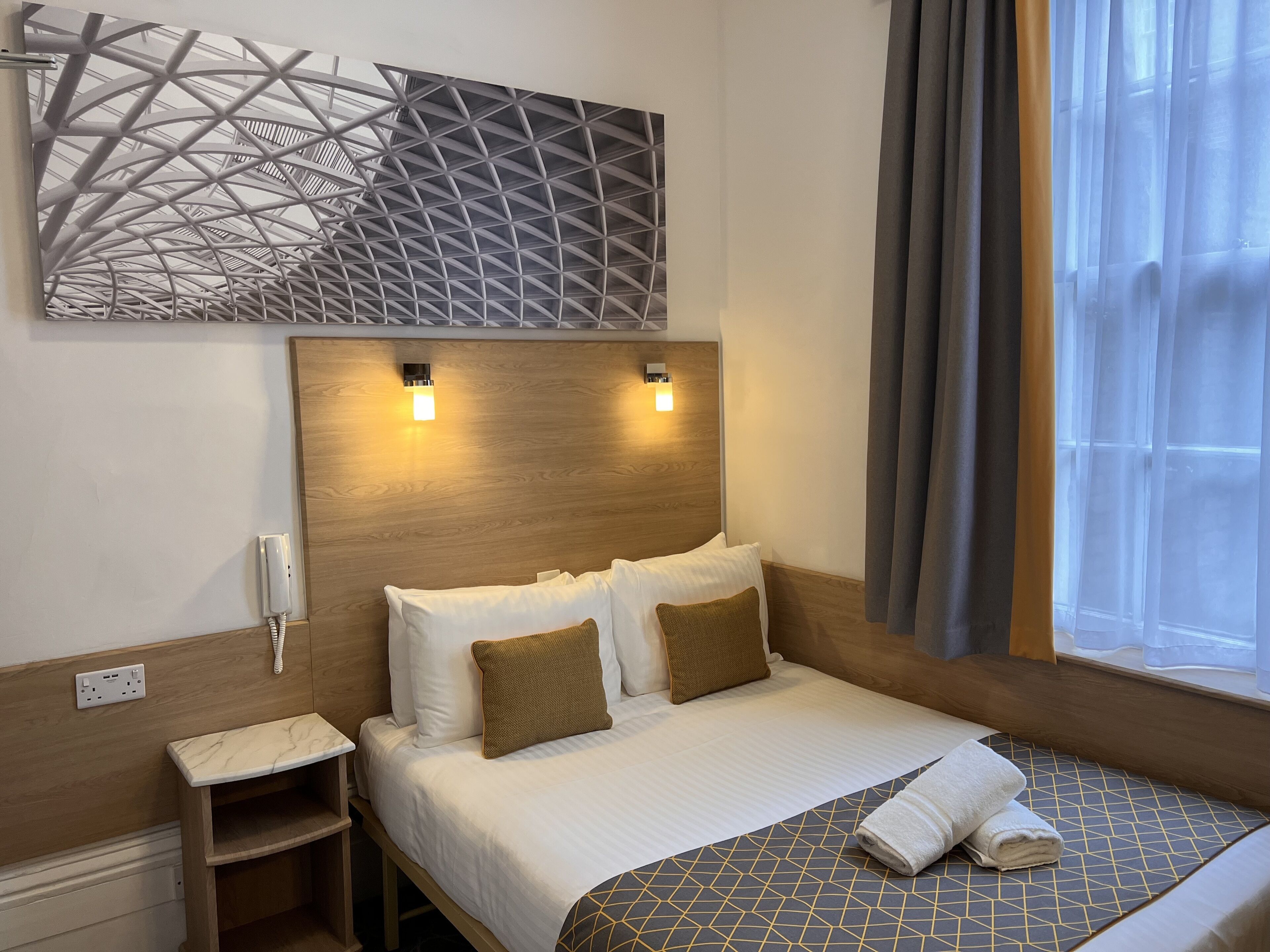 Quarto de hotel com cama, mesa de cabeceira e telefone fixado na parede.