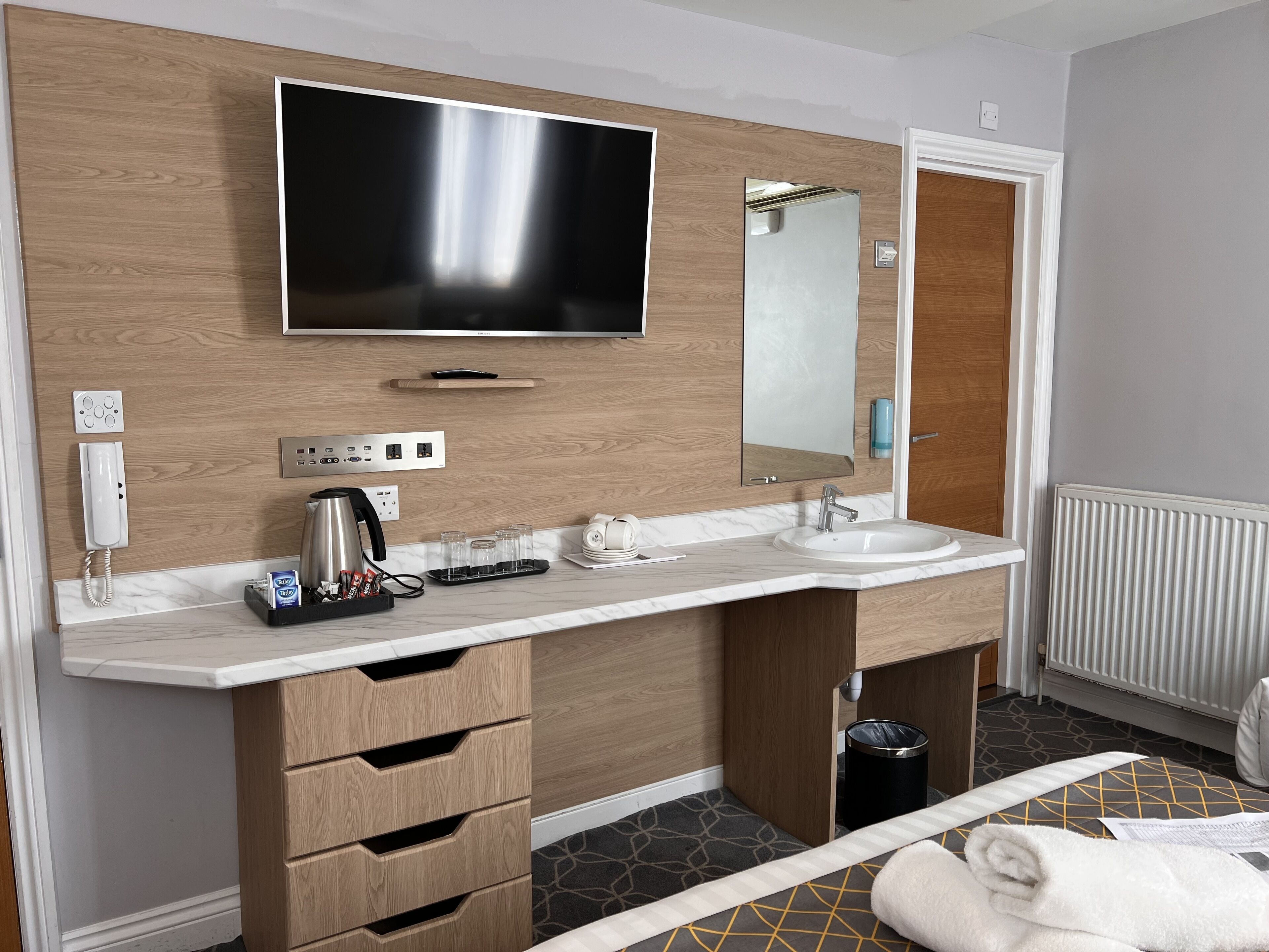 Ein modernes Badezimmer mit einem großen Spiegel, zwei Waschbecken, einem Fernseher und einer Kaffeemaschine.