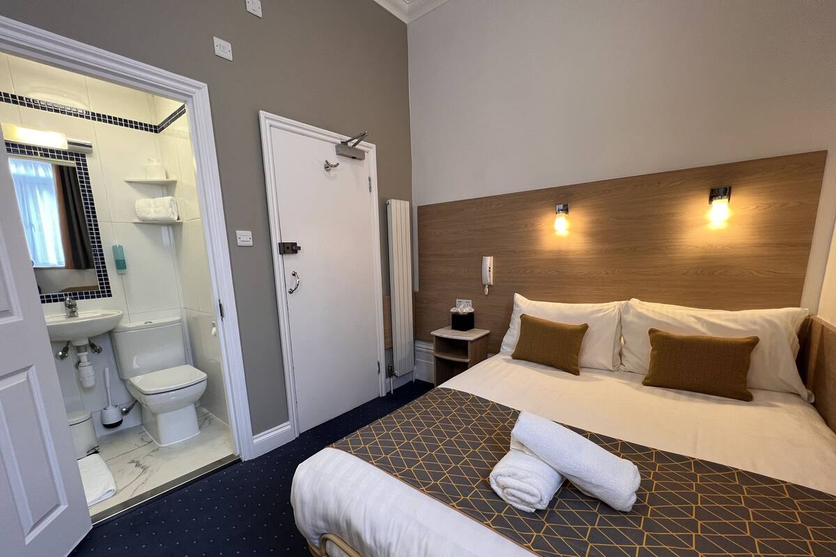 Ein Hotelzimmer mit Bett, Nachttisch und einem Badezimmer mit Toilette und Waschbecken.