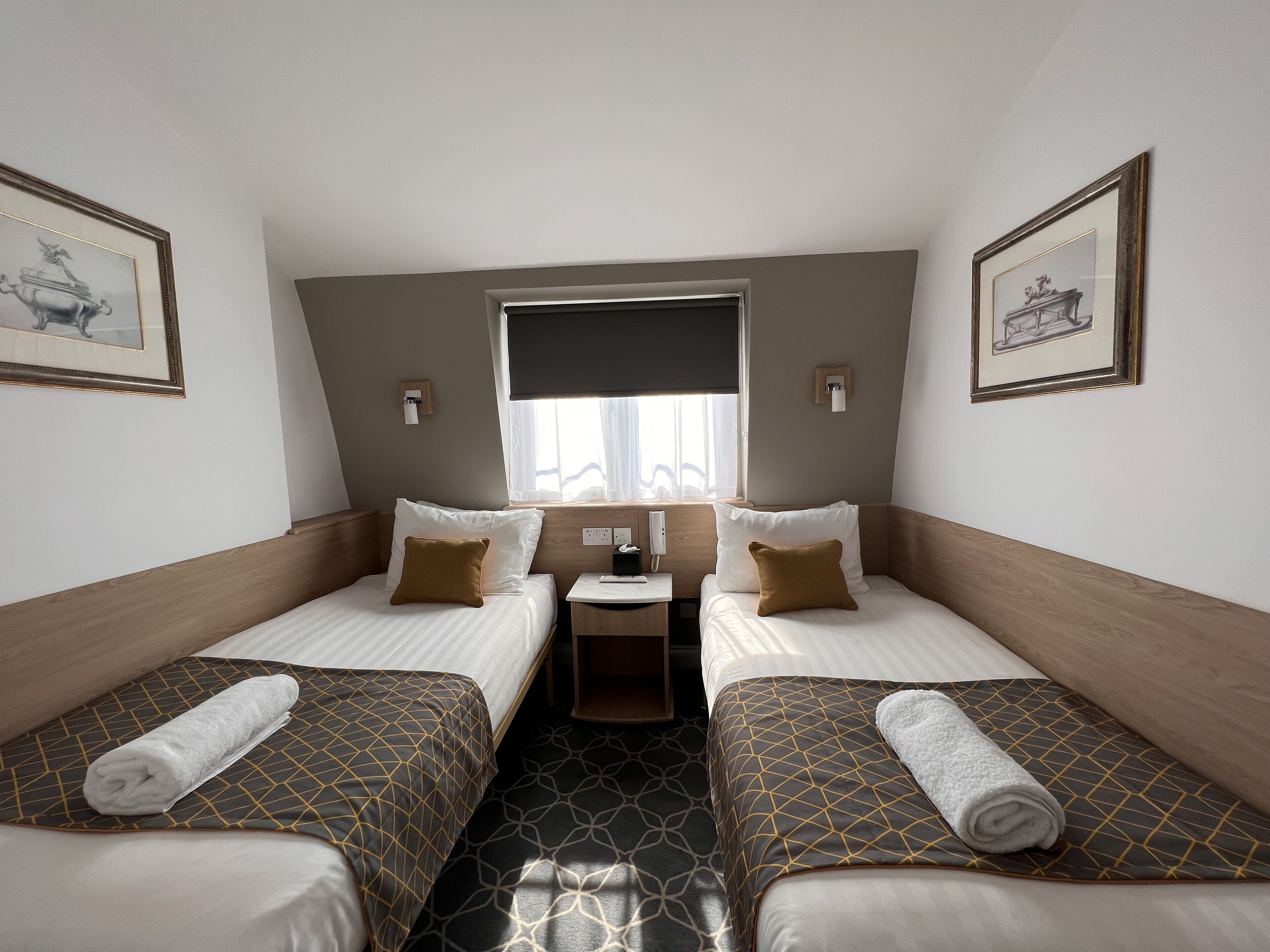 A hotel room with two beds, a small table, and a window with curtains.