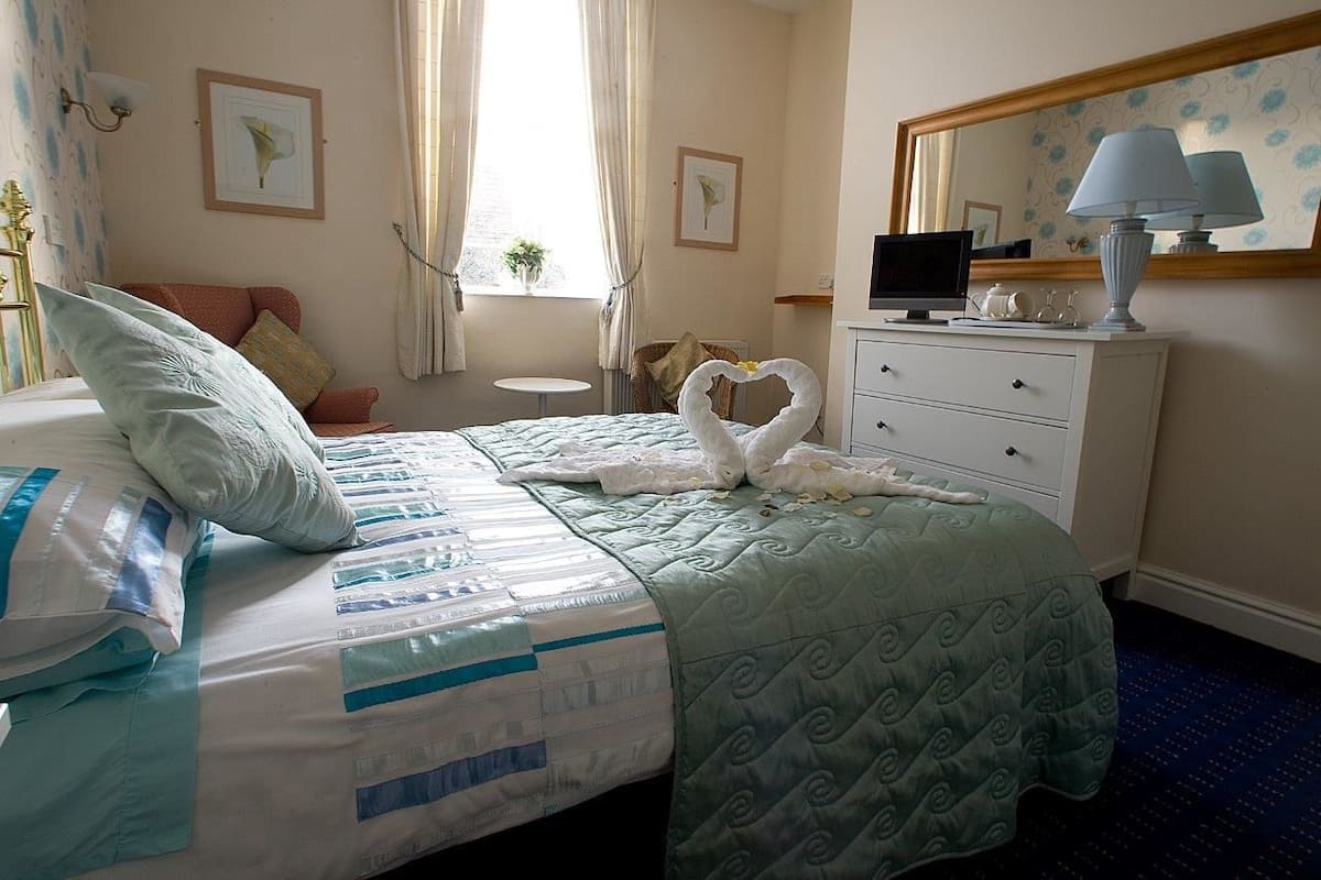 Una habitación de hotel con cama, tocador, televisión y ventana con cortinas.