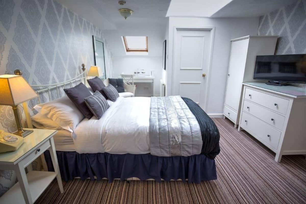 Una habitación de hotel con una cama, mesitas de noche, un escritorio, un televisor y un armario.