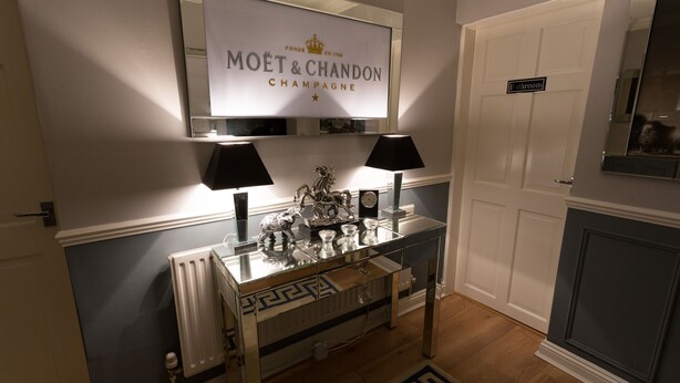A modern living room with a glass coffee table, two lamps, a decorative clock, and a sign above the table reading "MOËT & CHANDON CHAMPAGNE". - The Ascott (Manchester)