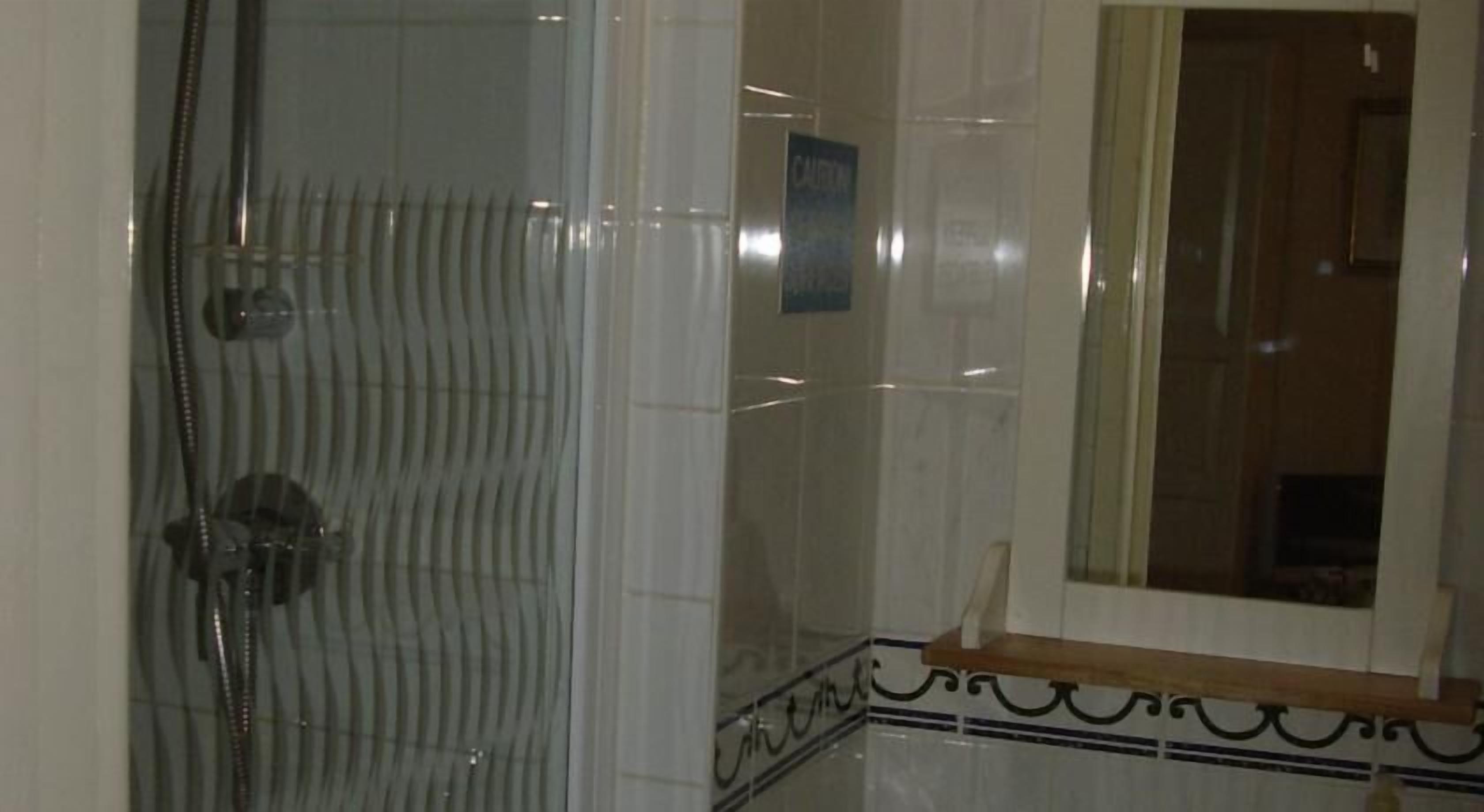 A bathroom with a glass shower enclosure, a mirror, and a tiled floor with a decorative border.