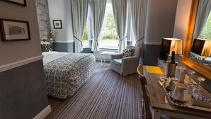 A hotel room with a large bed, a sitting area with a chair and table, and a view of the outdoors through the window. - The Ascott (Manchester)