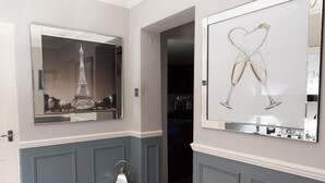 A hallway with a mirror reflecting the Eiffel Tower and a framed artwork of champagne glasses. - The Ascott (Manchester)