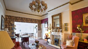 A spacious living room with a fireplace, a chandelier, and a large mirror. There are bookshelves and a dining area visible in the background. - The Ascott (Manchester)