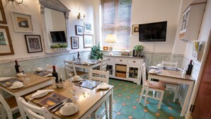 A dining area with a wooden table set for four, white chairs, a television mounted on the wall, and a window with blinds. - The Ascott (Manchester)