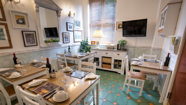 A dining area with a wooden table set for four, white chairs, a television mounted on the wall, and a window with blinds. - The Ascott (Manchester)