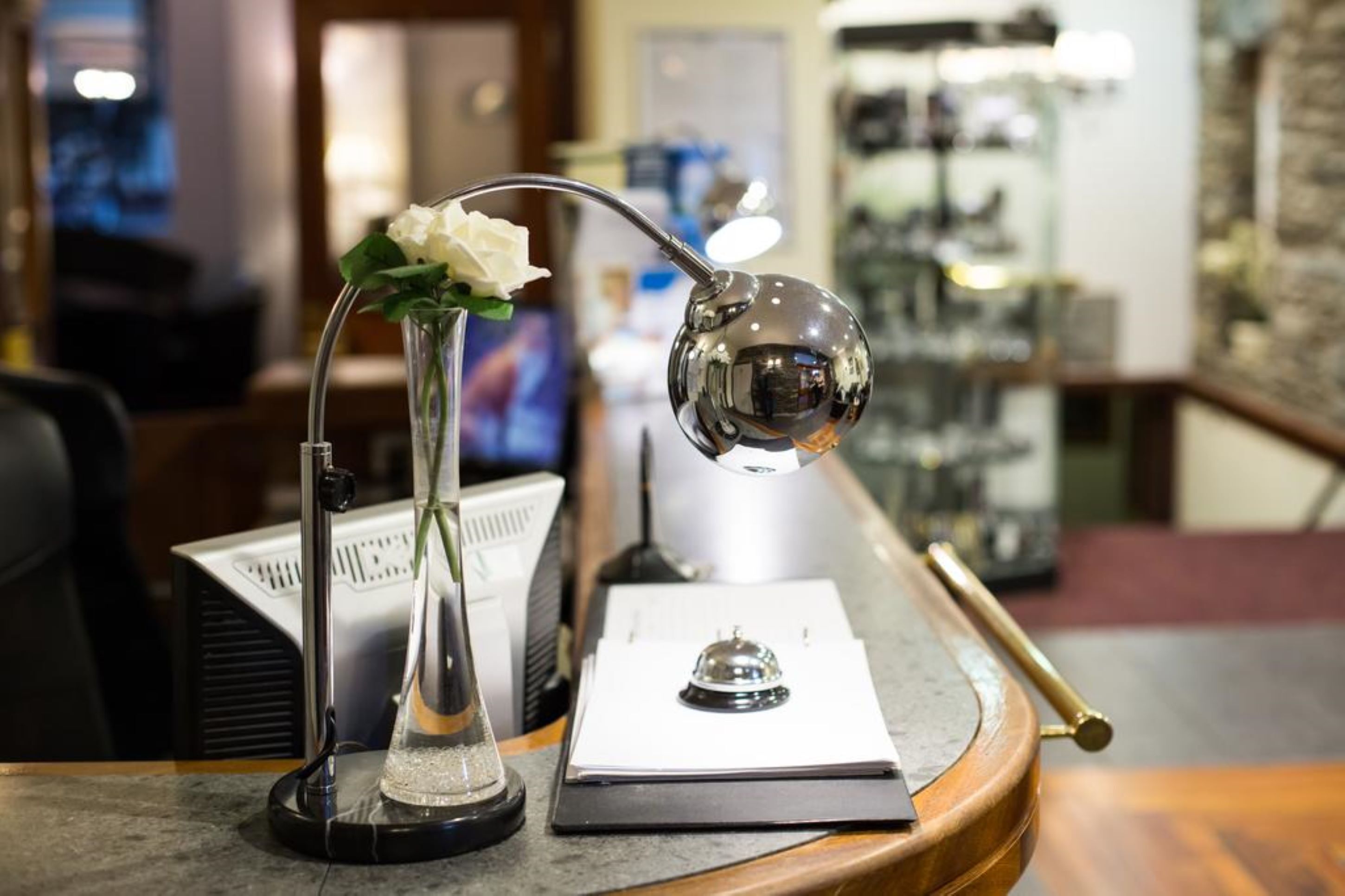 A desk with a vase of white flowers, a desk lamp, and a clipboard.
