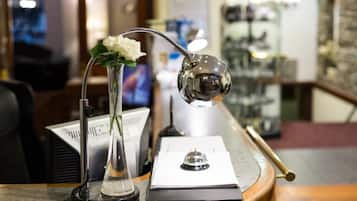 A desk with a vase of white flowers, a desk lamp, and a clipboard.