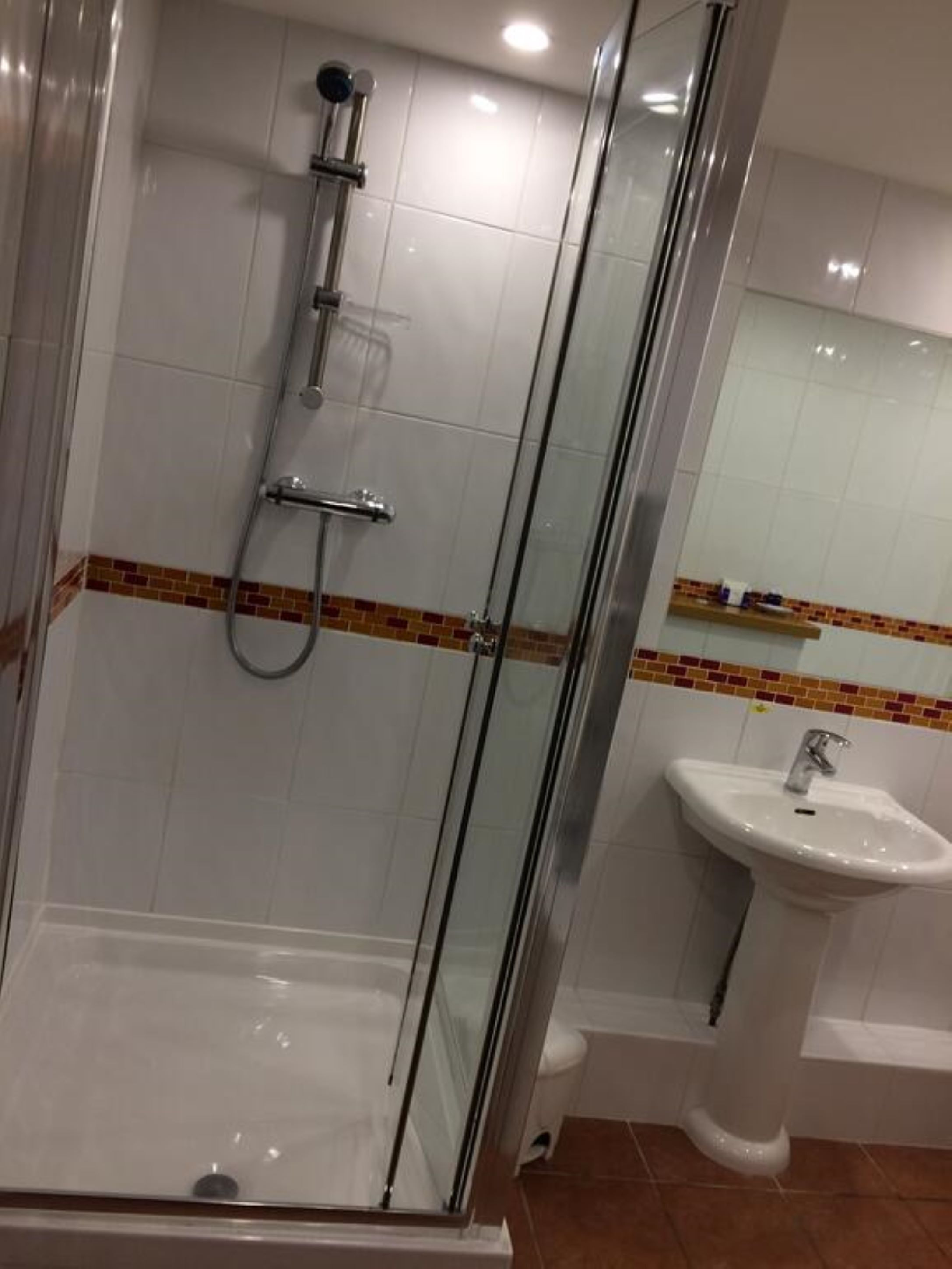 A glass-enclosed shower with a handheld showerhead, a wall-mounted faucet, and a tiled floor.
