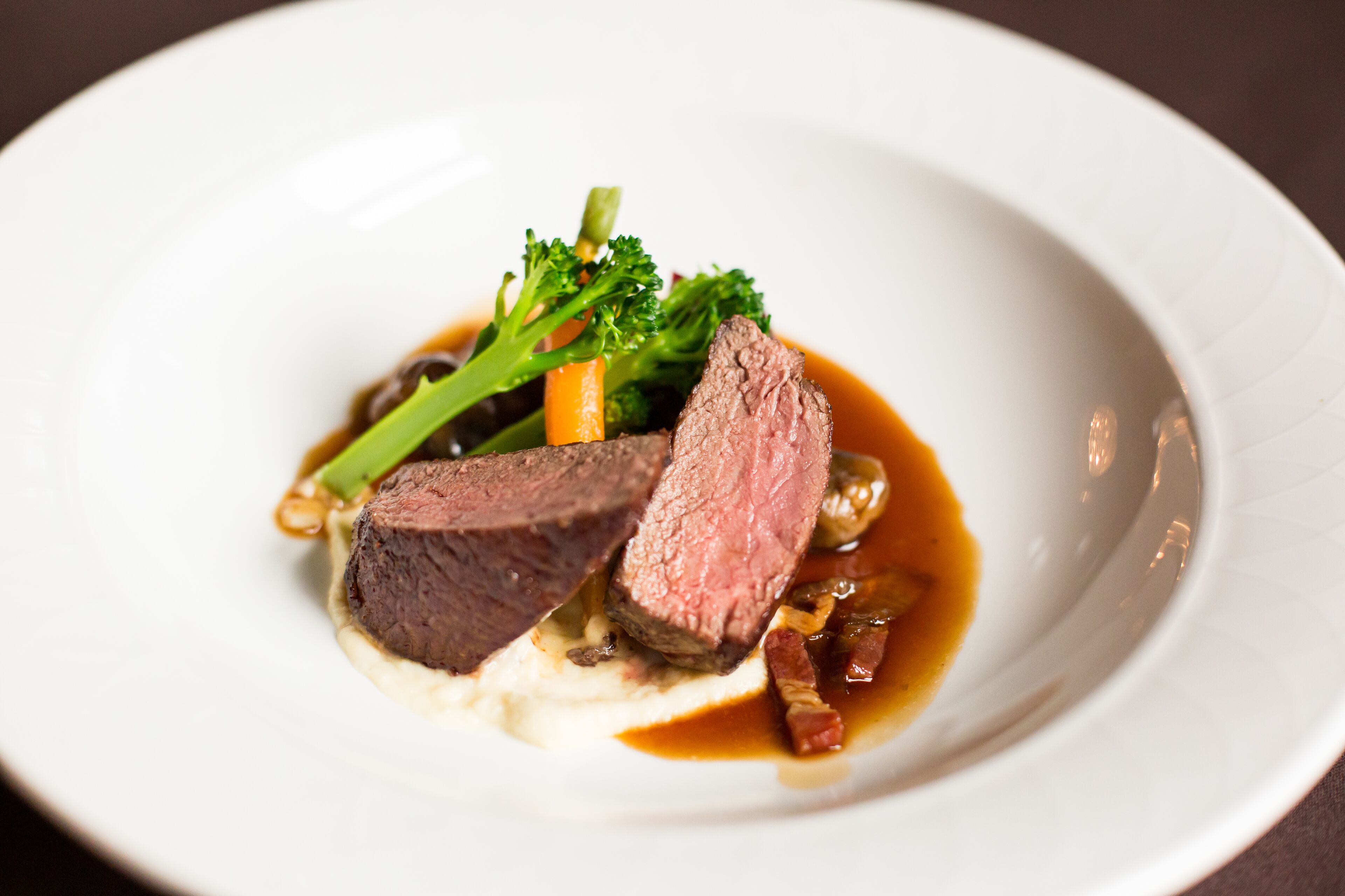 En hvid tallerken med et stykke steak, broccoli og sauce.