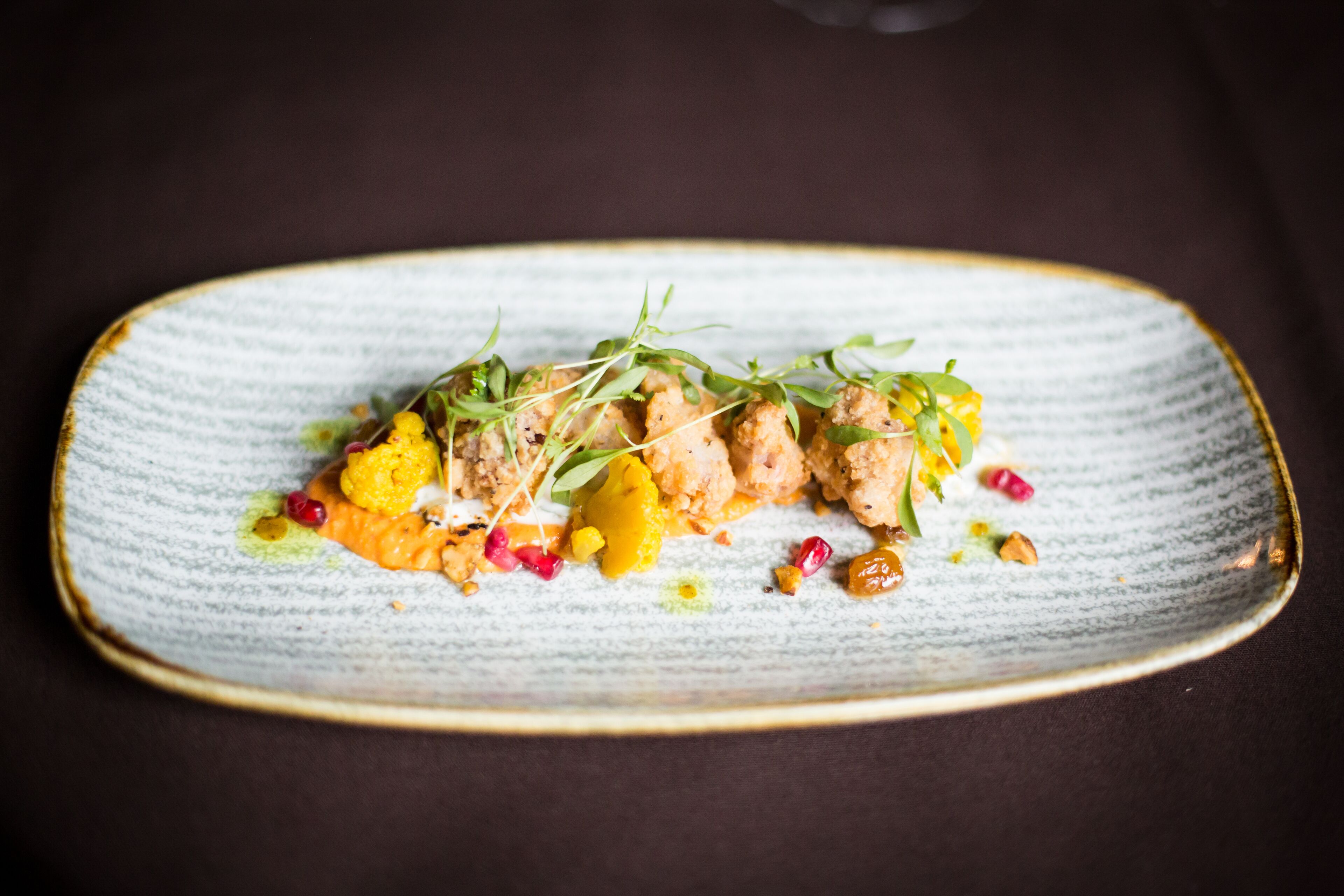 A plate of food with various colorful garnishes and a textured ceramic plate.