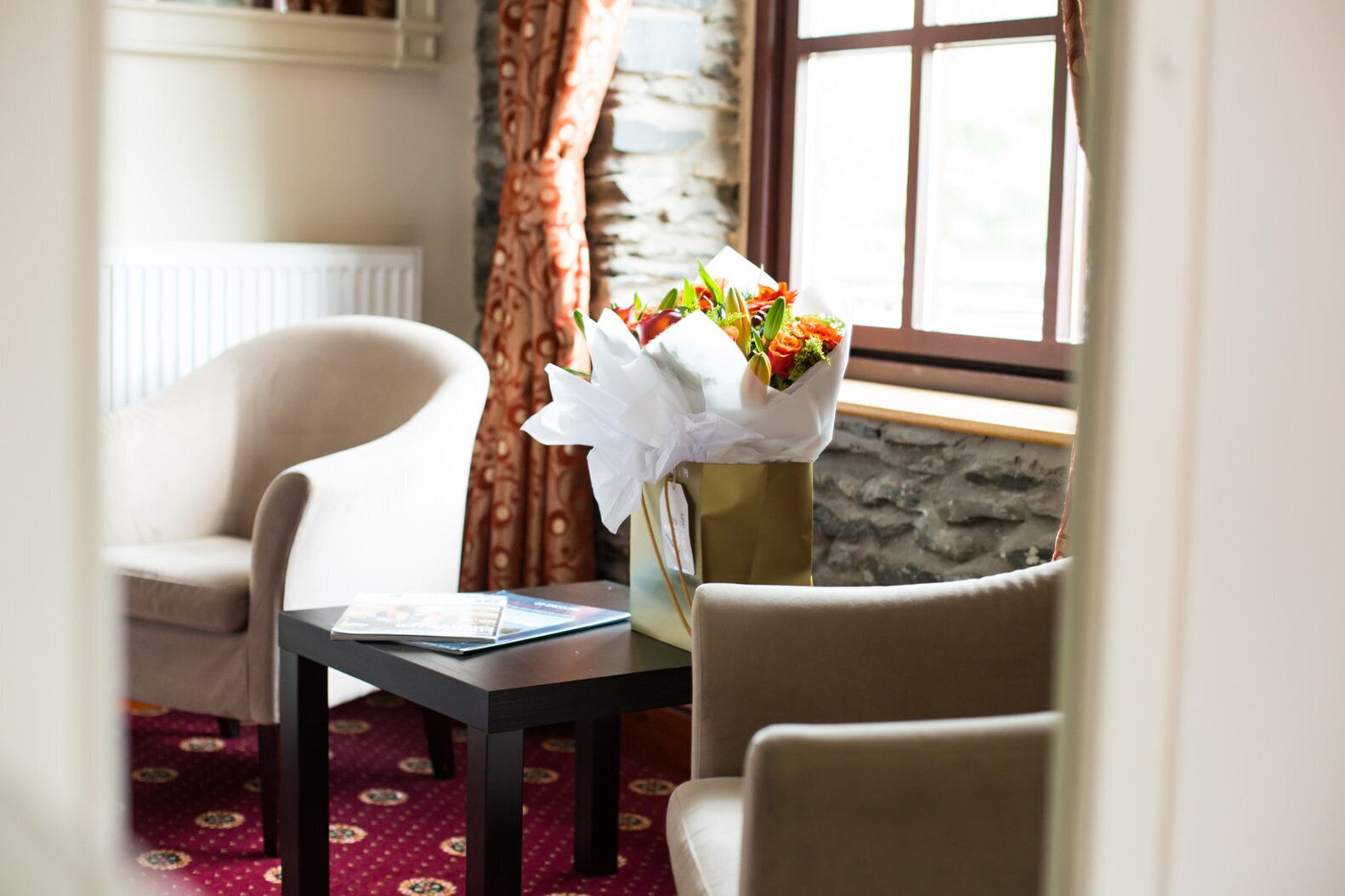 A room with a table, two chairs, a vase with flowers, a window, and a patterned carpet.