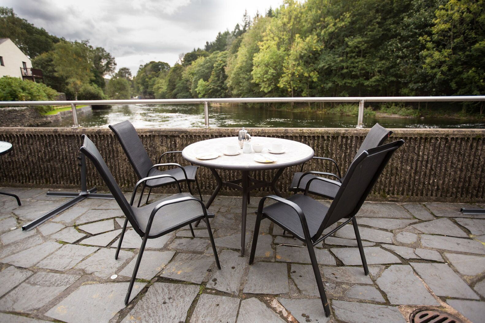 Un patio al aire libre con una mesa redonda y cuatro sillas, con vistas a un río y rodeado de vegetación.