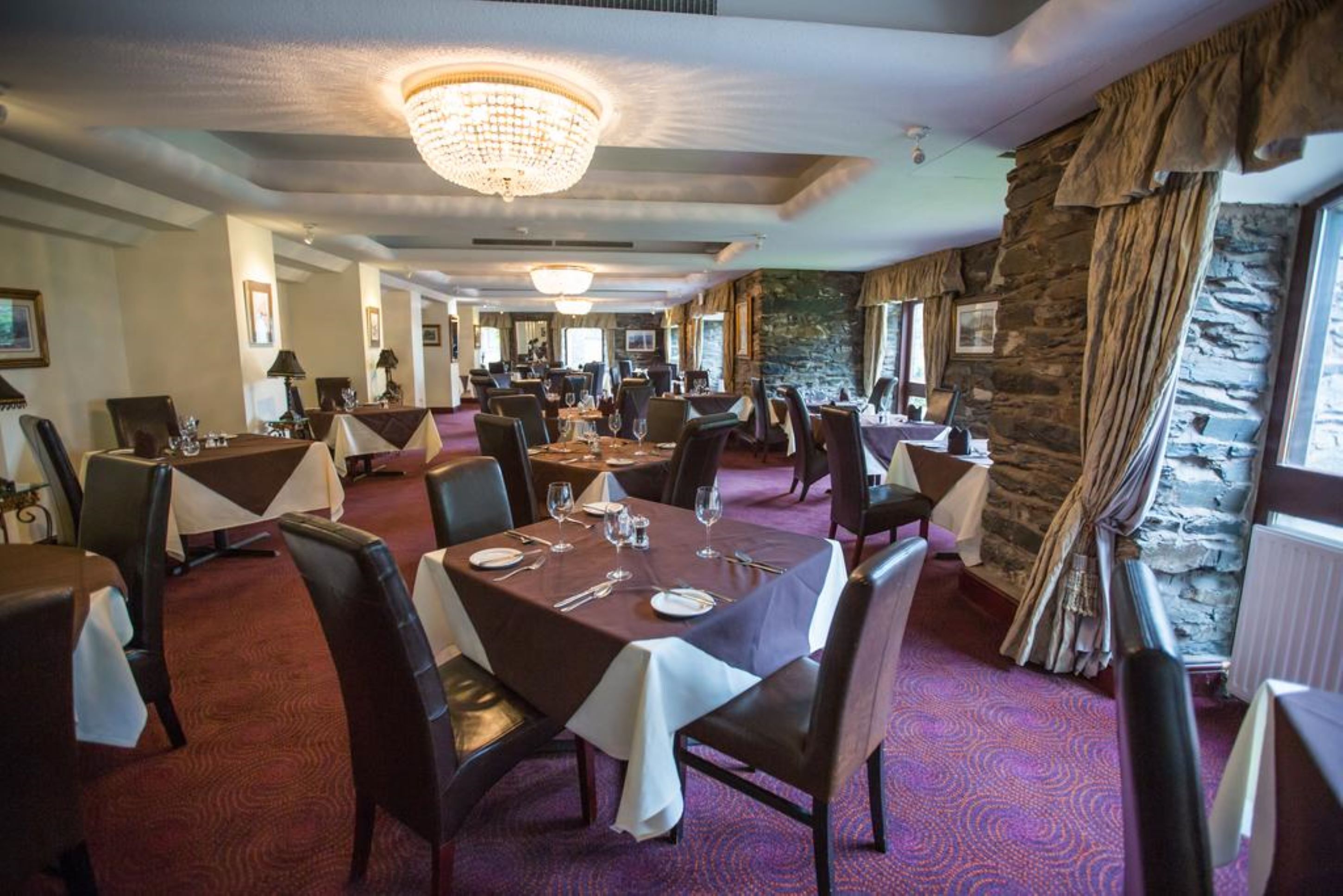 Een restaurant met meerdere eettafels, een kroonluchter, stenen muren en ingelijste foto's aan de wanden.