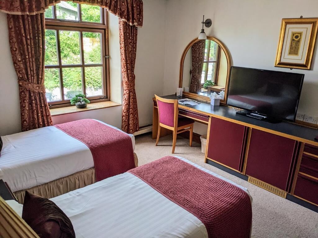 Een hotelkamer met twee eenpersoonsbedden, een bureau met stoel, een televisie en een raam met gordijnen.