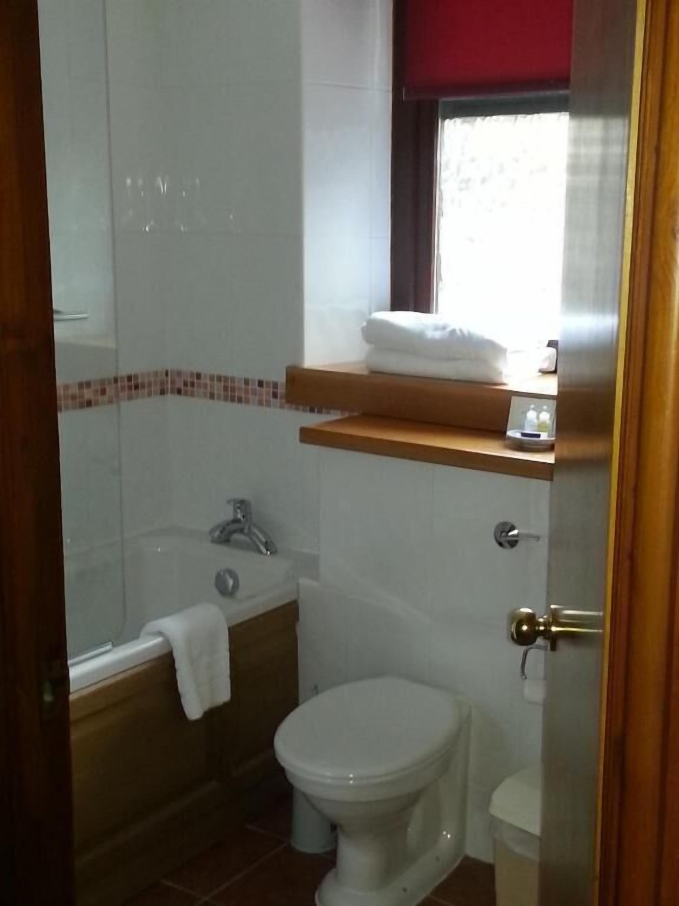 Un baño con bañera, inodoro y ventana con cortina roja.
