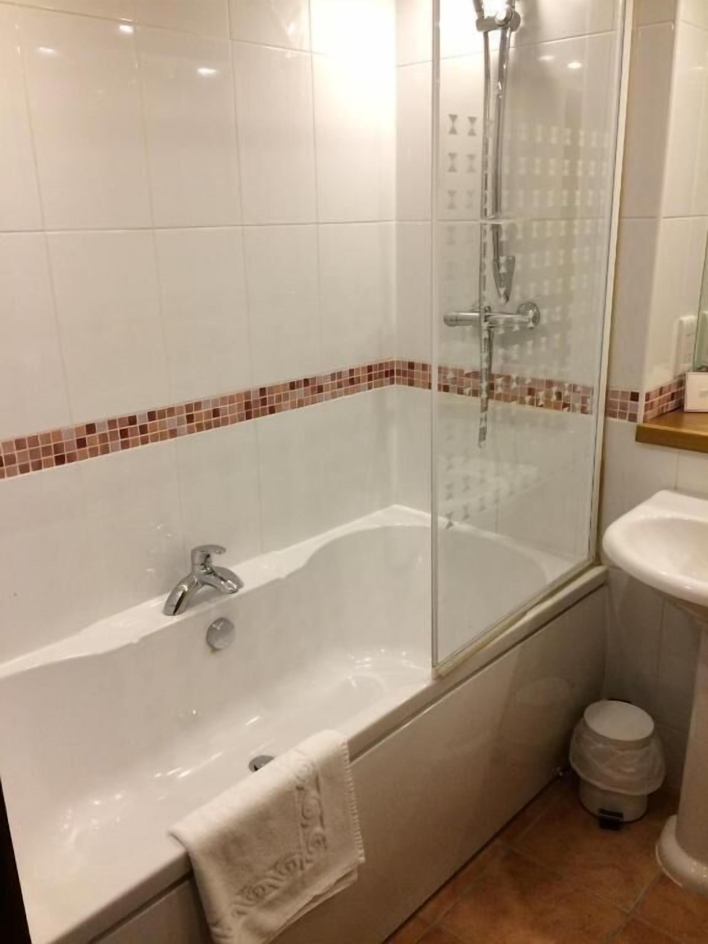 Et badeværelse med et hjørnebadekar med glasvægge, en hvid vask og et flisegulv.