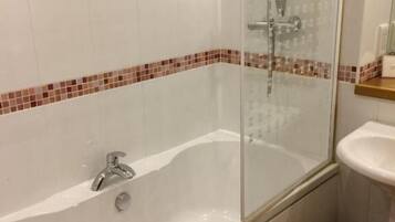 A bathroom with a glass-enclosed bathtub, a white sink, and a tiled floor.