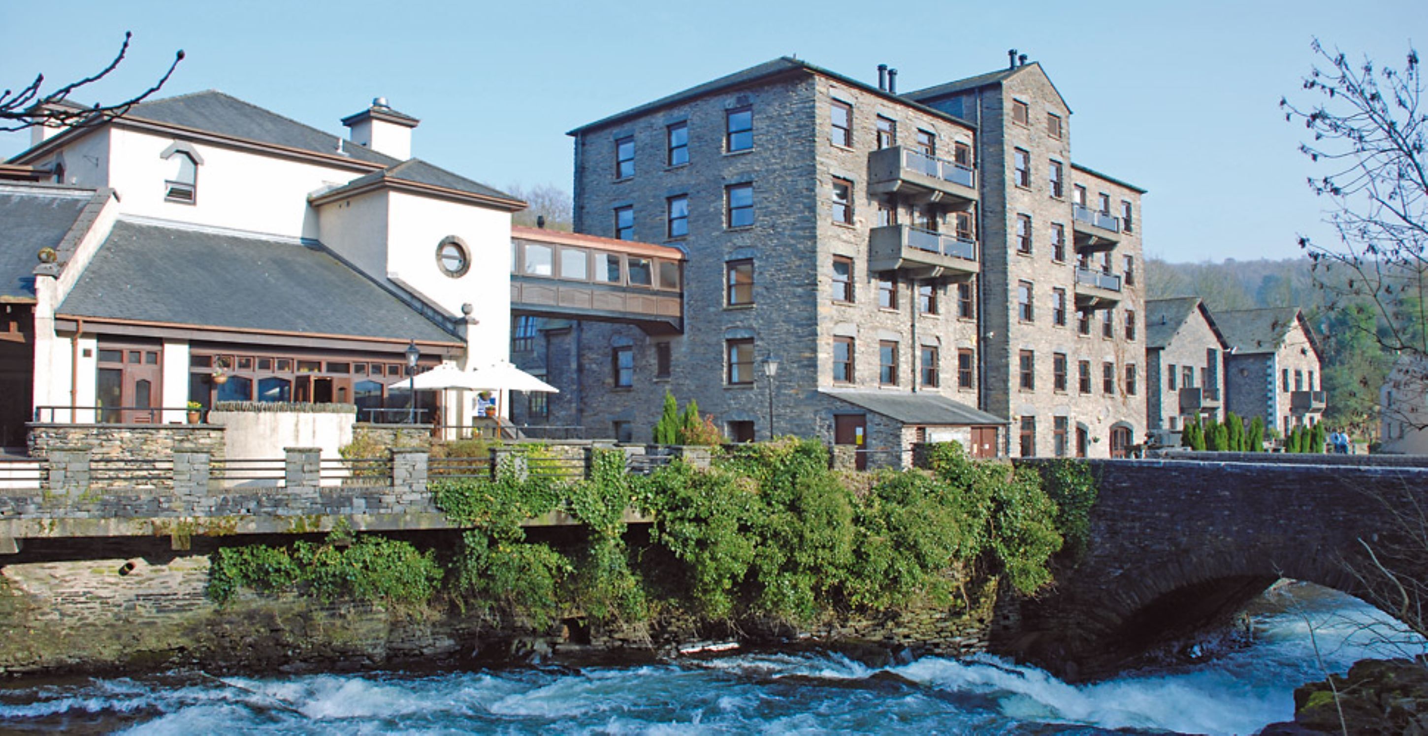 A stone bridge over a river with buildings on either side, including a white building with a clock and a stone building with balconies.
