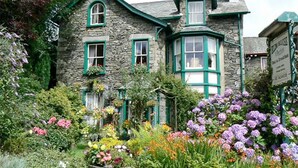 En bygning i sten med grønne vinduesrammer, en have med forskellige blomster og et skilte