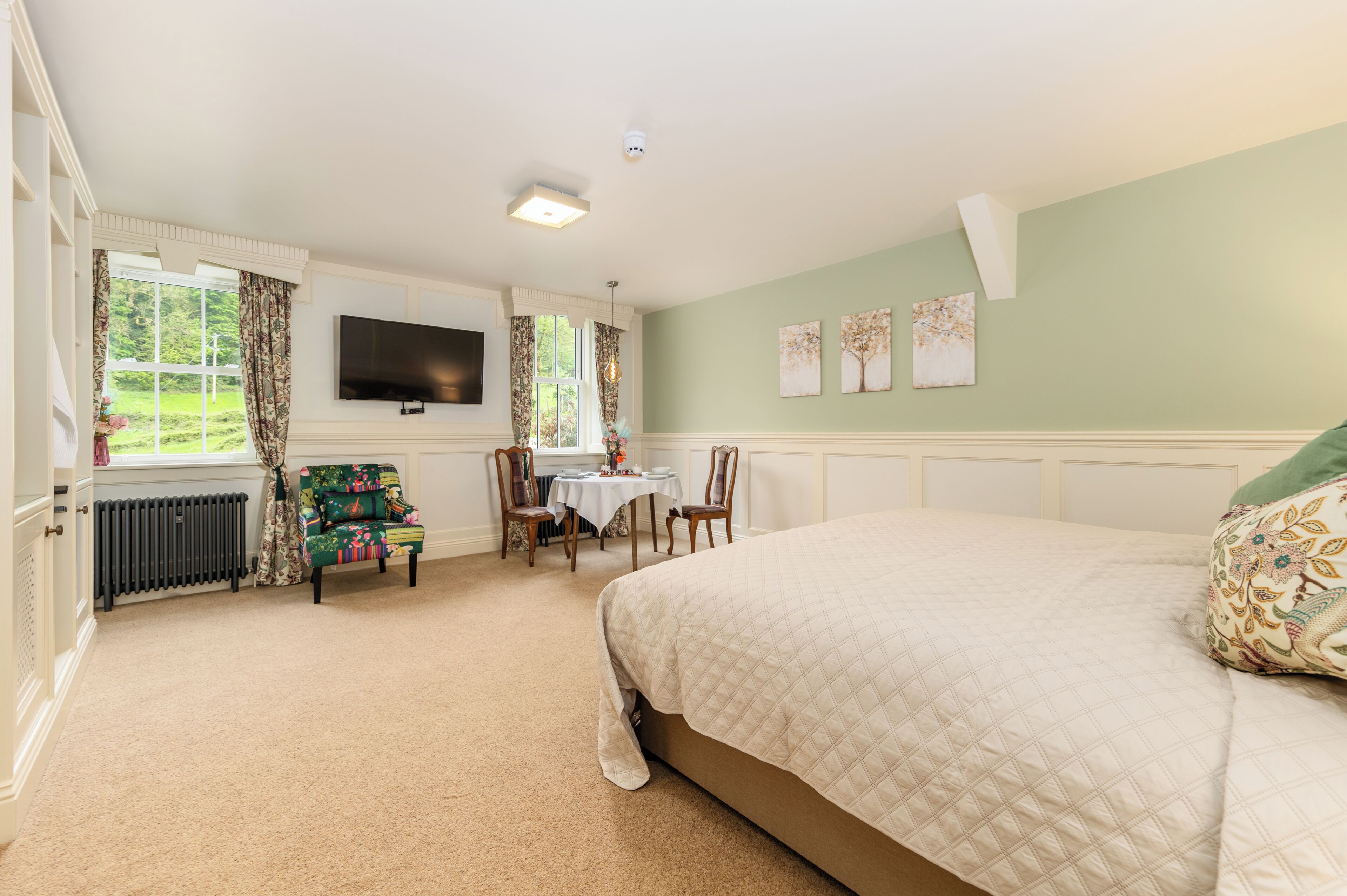 A bedroom with a bed, a television, a table with chairs, and a window with curtains.